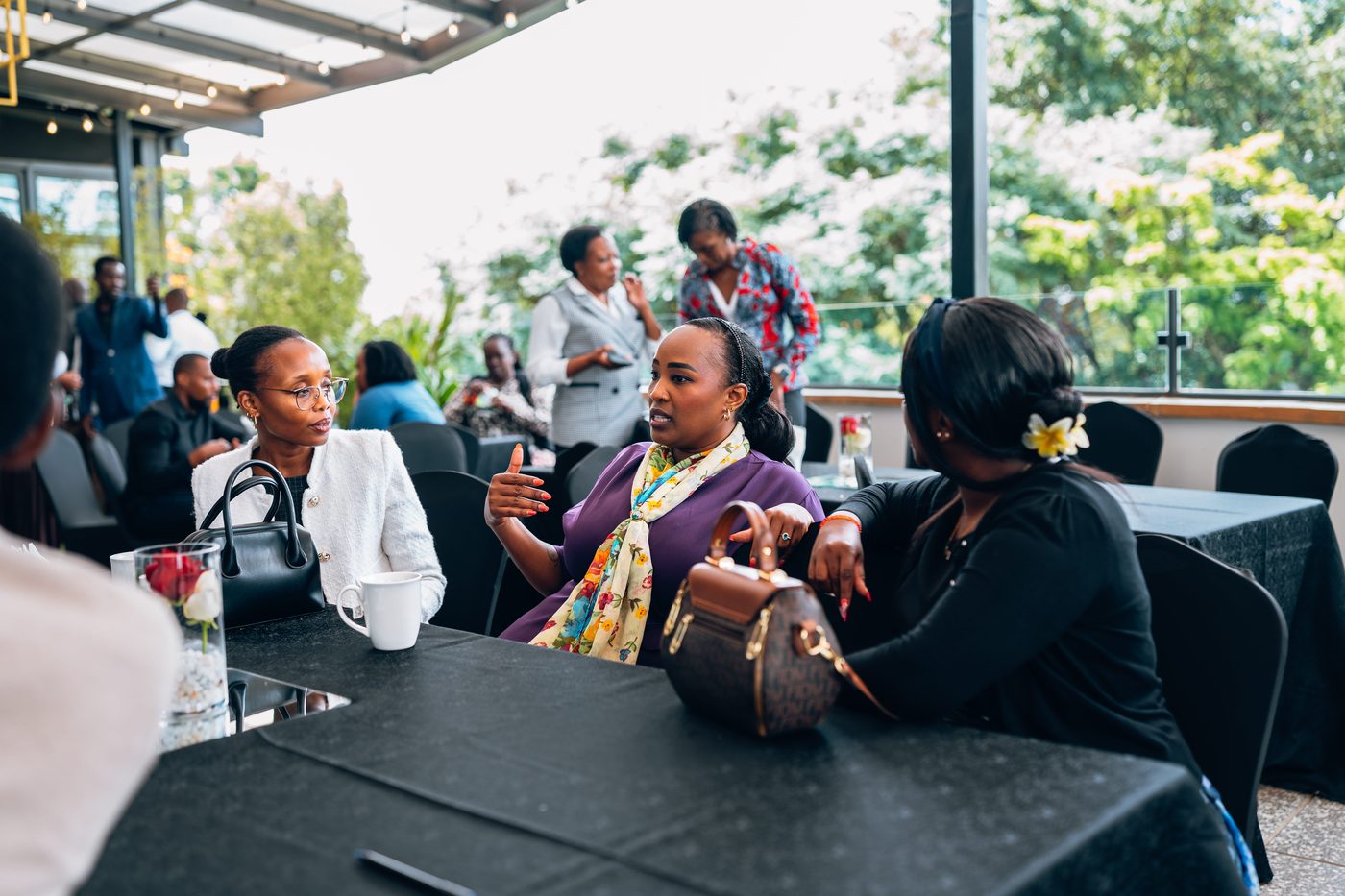 Three women in conversation at rooftop event, daylight