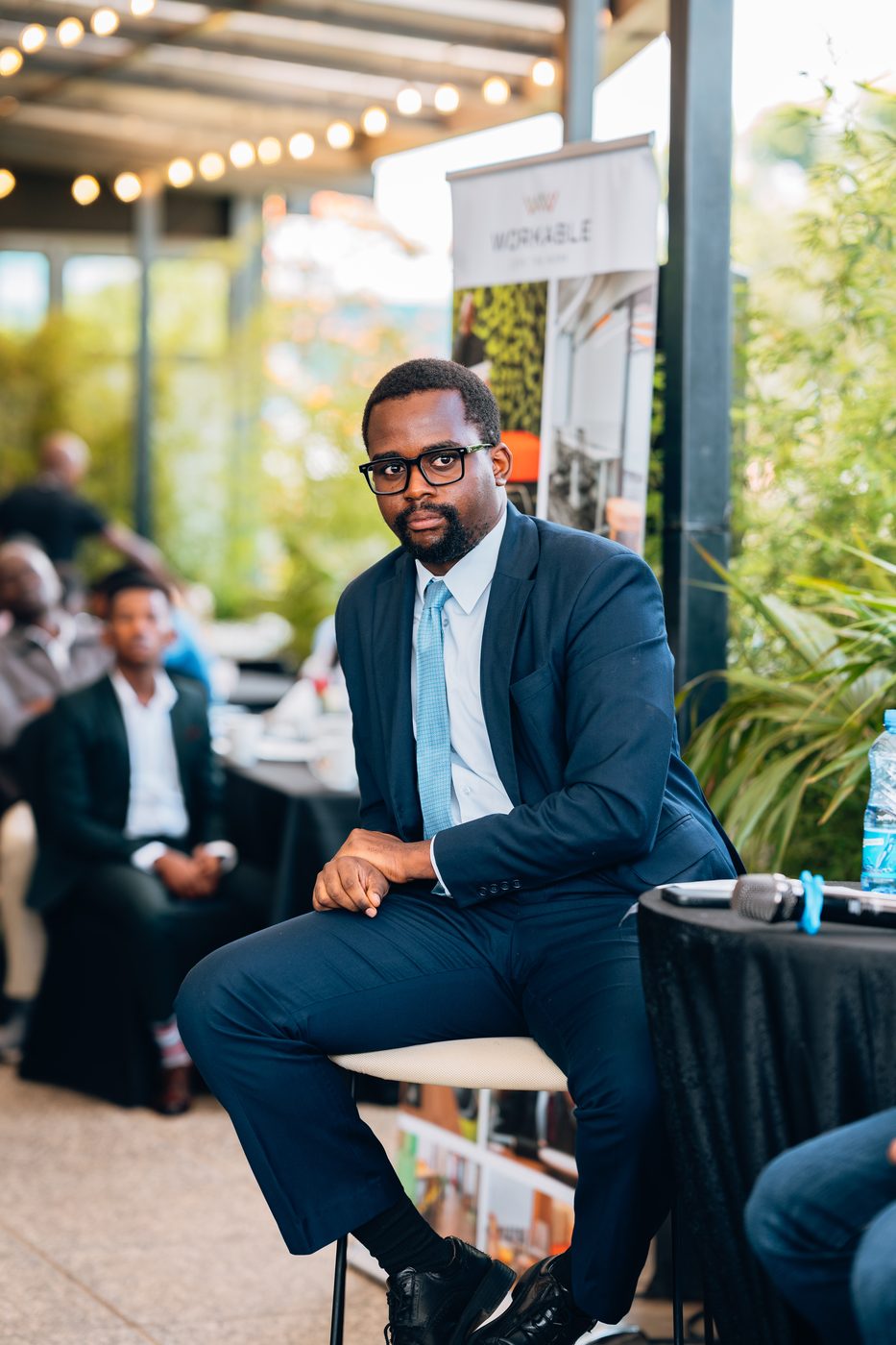 Formal seated portrait of a man in dark suit and blue tie during the corporate event, Workable banner visible