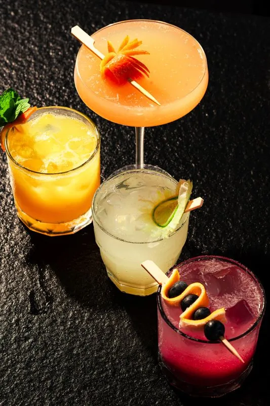Three colourful mocktails photographed from above on dark stone