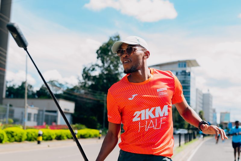 Runner in orange 21KM Half vest holding a selfie stick mid-race