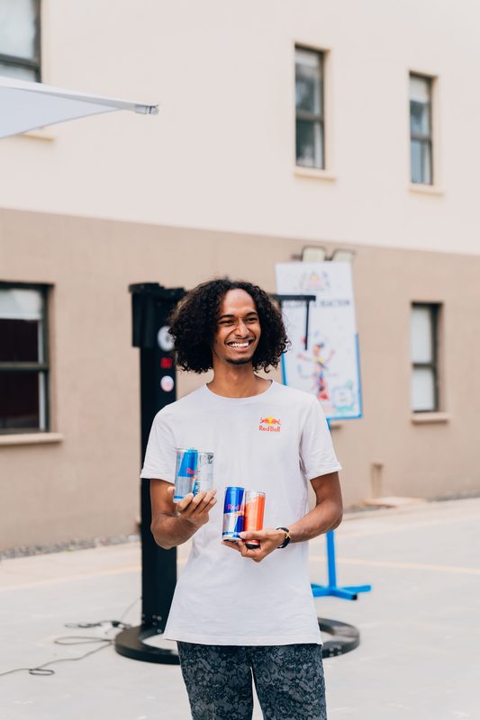 Brand ambassador holding three Red Bull cans — original, Sugar Free, and Red Edition