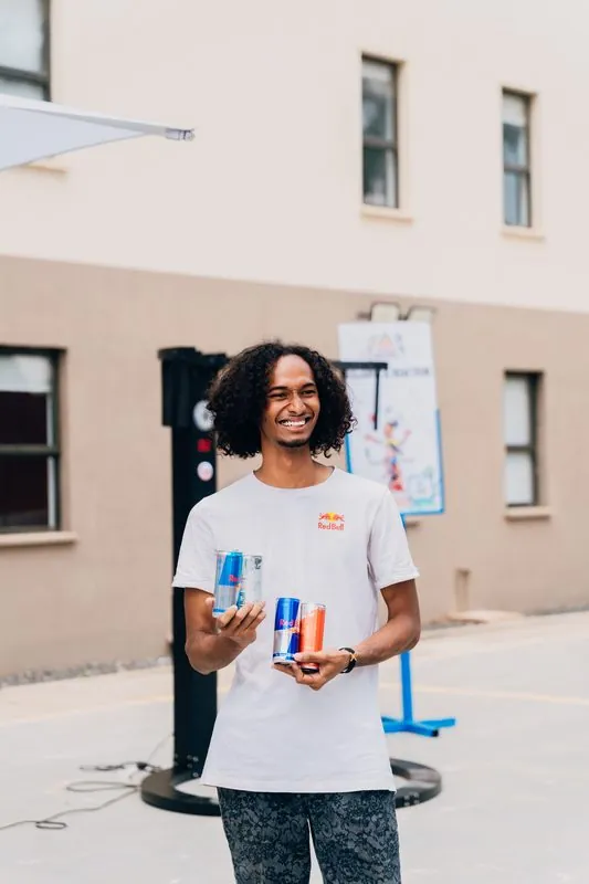 Brand ambassador holding three Red Bull cans — original, Sugar Free, and Red Edition