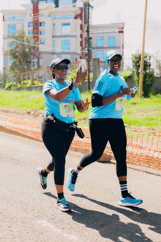 Two women running together, one holding a phone selfie-style during the race
