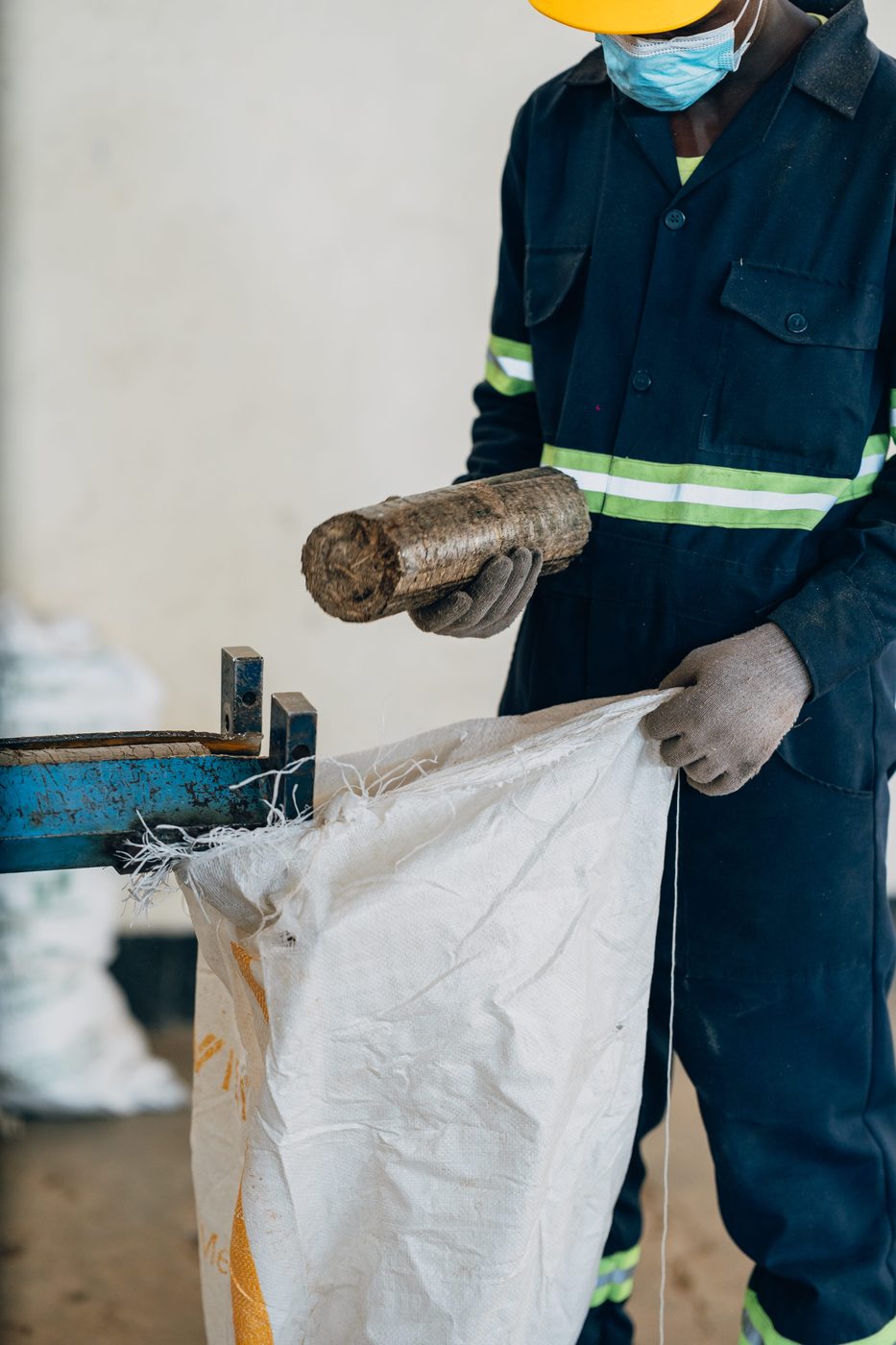Worker holding a freshly pressed cylindrical briquette over an open white sack